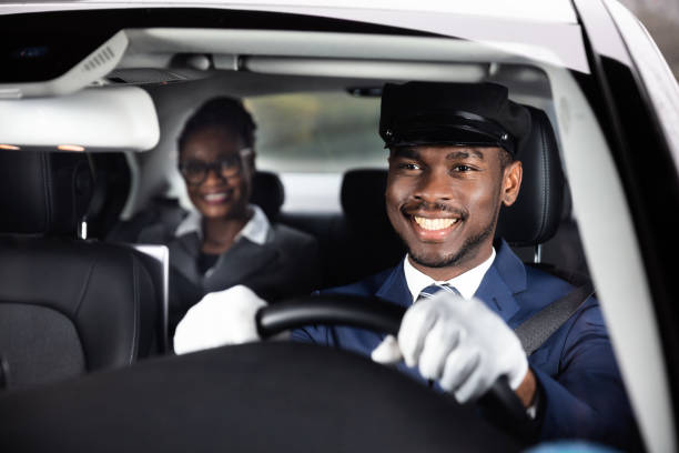 businesswoman sitting behind happy african male chauffeur driving car